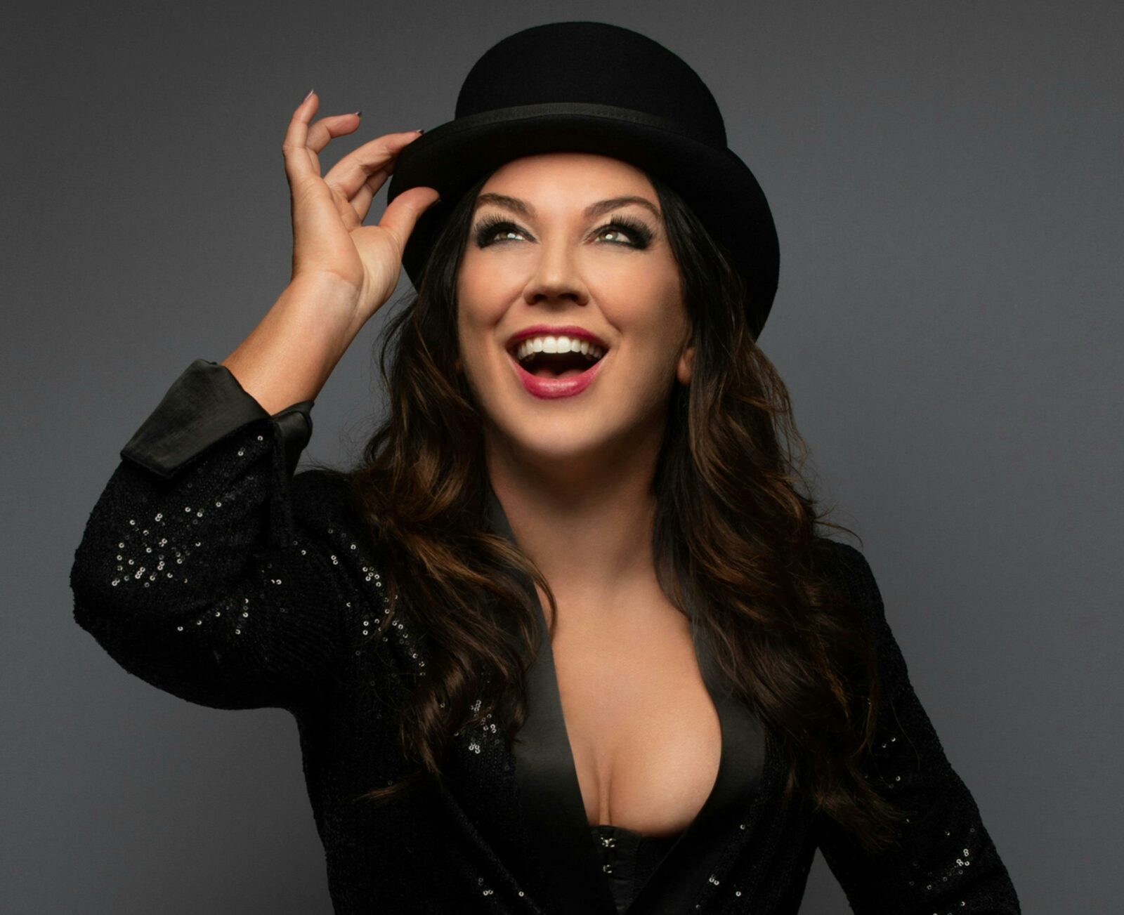 A performer in top hat and jacket is smiling and holding on to her hat