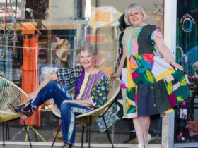 Two women one seated and one standing wearing patchwork upcycled clothng