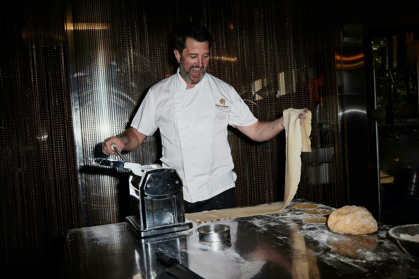 A smiling chef rolls pasta in a commercial kitchen at Josef Chromy Restaurant