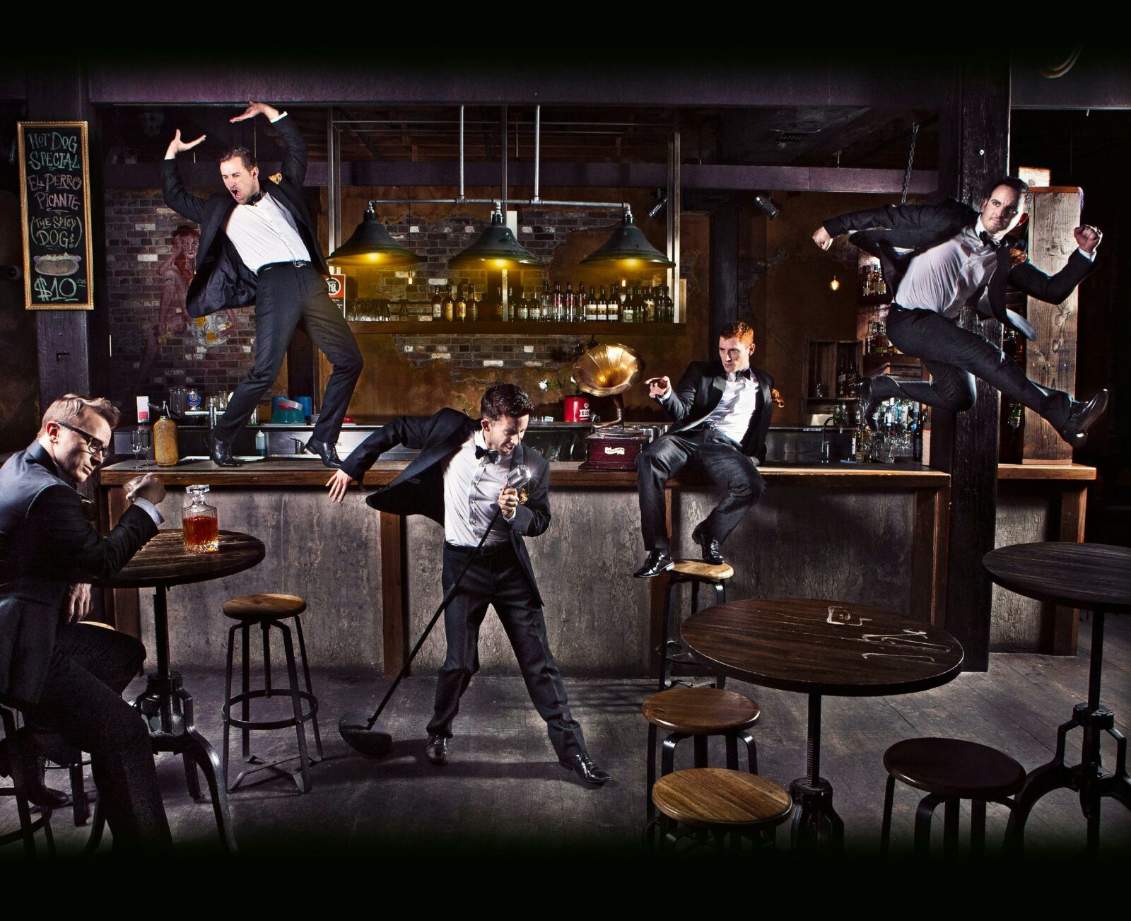 A group of dancers in tuxedos are in various positions in a bar