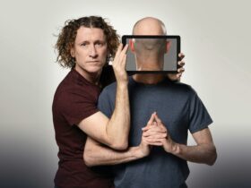 Two men facing the camera. One has a ipad in front of his face, showing the back of his head