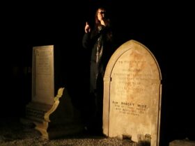 A woman standing in front of a gravestone at night, in a Voices from the Graves performance.
