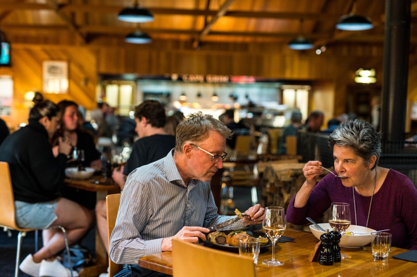 Couple eating a meal in Kauri Bistro with other patrons & Cape Grim Grill visible in background