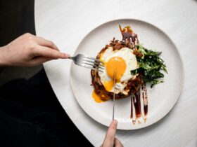 Pork Sword Breakfast - two hands holding cutlery, cutting into a fried egg breakfast on a plate