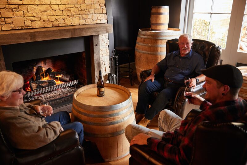 Three guests enjoying a drink in front of the warm fireplace at Drink Tasmania Tasting House.