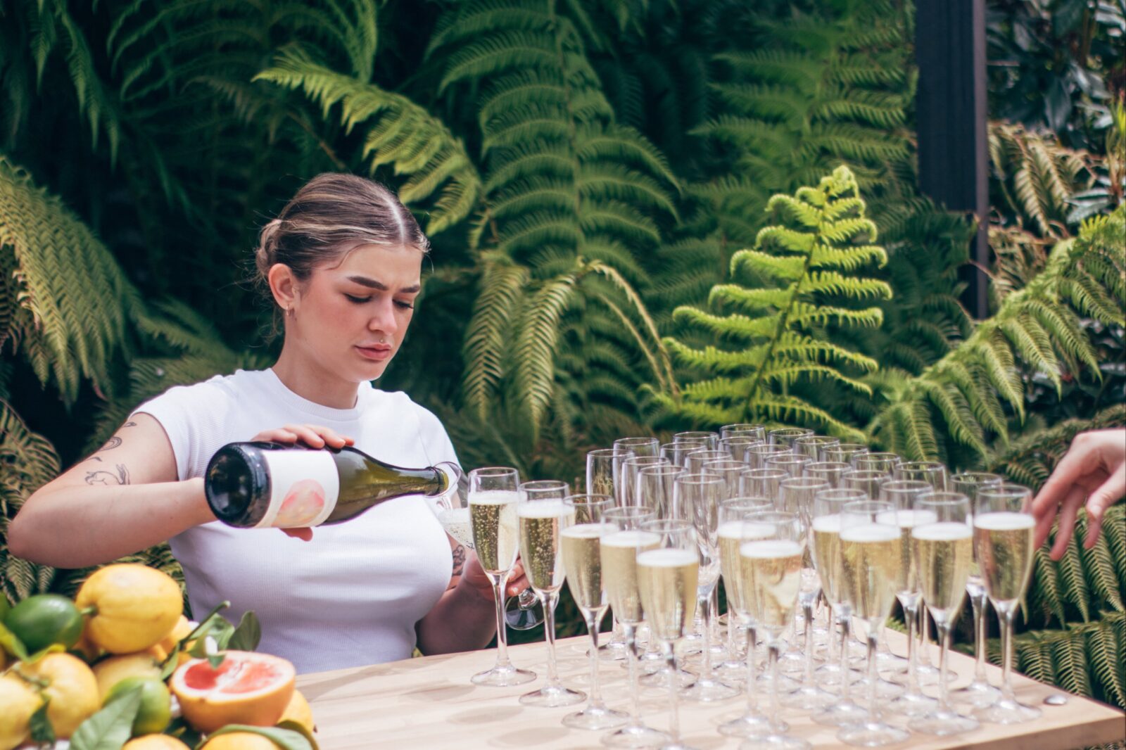 A caucasian woman in her twenties pours sparkling wine into champagne flutes