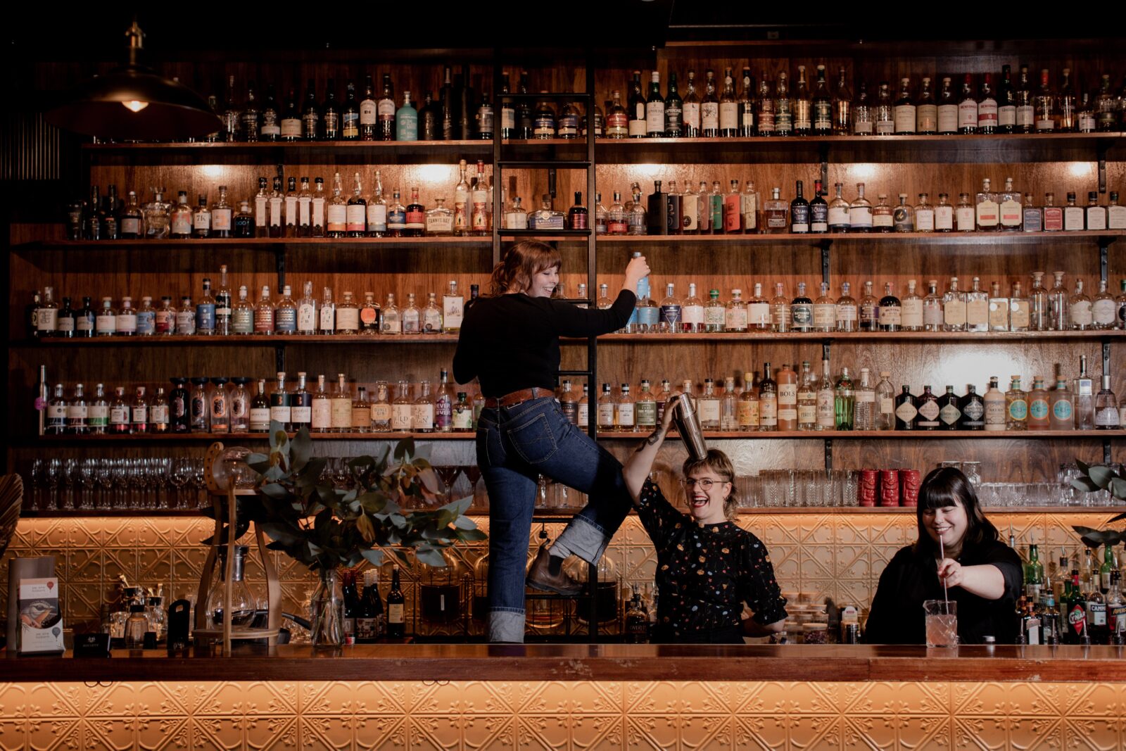 Cocktail bar, three female bartenders making drinks infront of a large backbar - gin and whisky