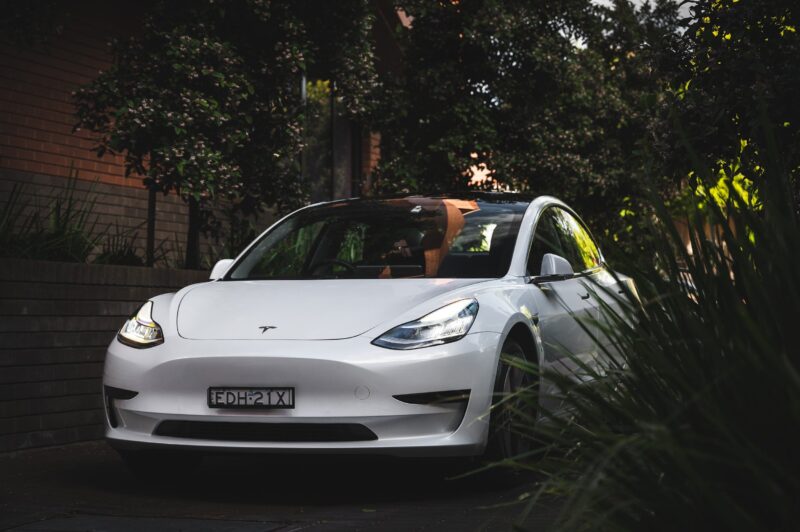 a white tesla parked with trees around waiting to be hired