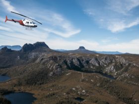 Our red & white Bell Jetranger helicopter flying past Cradle Mountain and Crater Lake