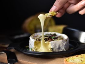 A brie style cheese is beautifully displayed on a plate topped with nuts and herbs.