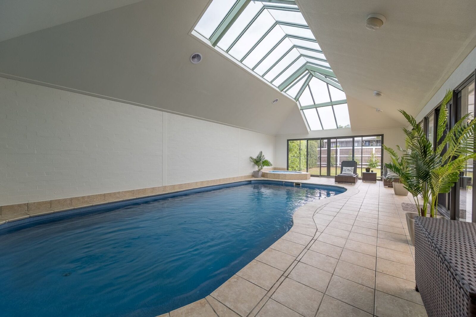 Image of indoor heated swimming pool with skylights above and windows at end of pool. Tiled surround