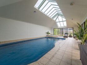 Image of indoor heated swimming pool with skylights above and windows at end of pool. Tiled surround