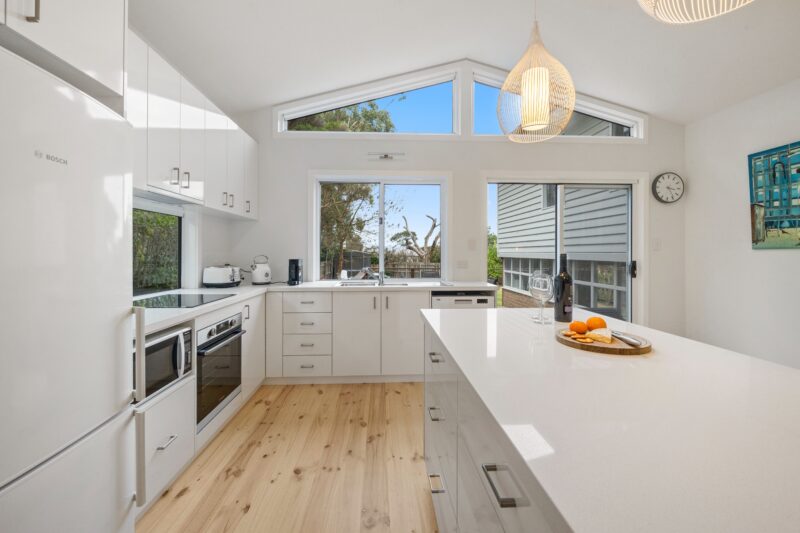 All white kitchen with timber floors, island bench and windows facing East