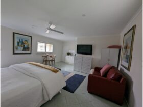 King bed with white doona. Red leather lounge to the right hand side with view to kitchen