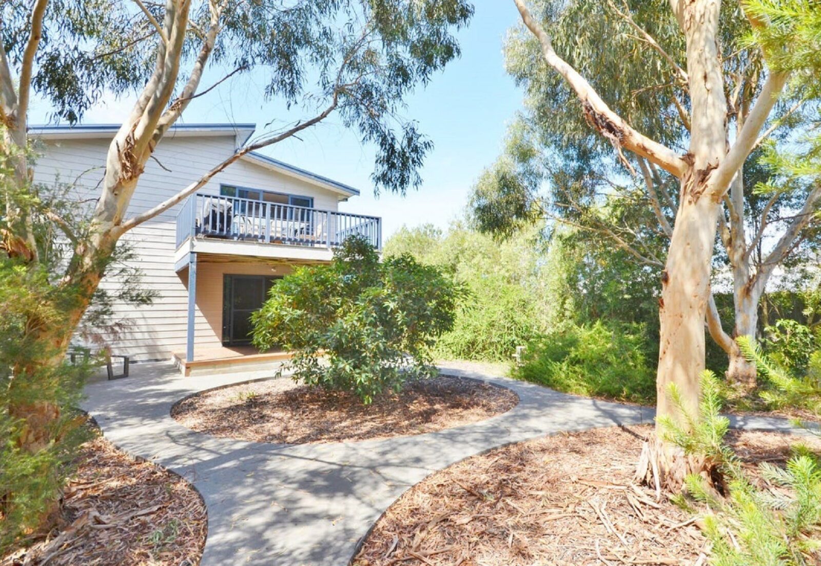 Image of two storey weatherboard house in treed setting showing path through mulch and native garden