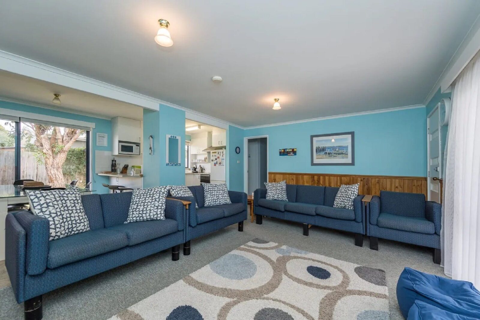 Very blue room with large couches, rug, looking beyond to kitchen and meals area