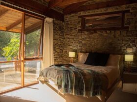 Bedroom 3 with queen bed against a rock wall, floor to ceiling glass windows