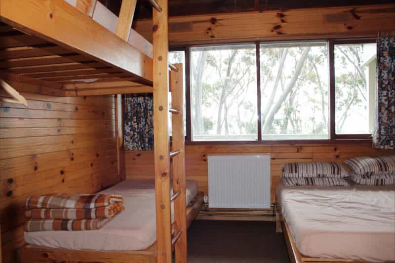 A room at Edski Lodge, a double bed with a set of single bunks with a view of snowgums out the windo
