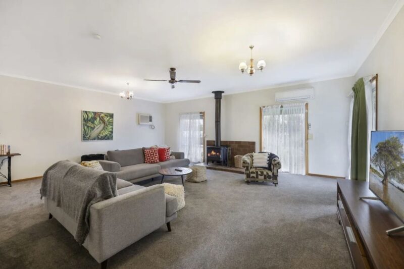 Living area with grey sofa and carpet. White walls, fireplace and ceiling fan.