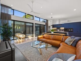 View of living room with large leather couch and glass coffee table with kitchen in background