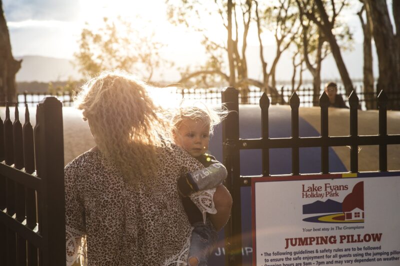 A mother with a young child entering through the gates into the jumping pillow