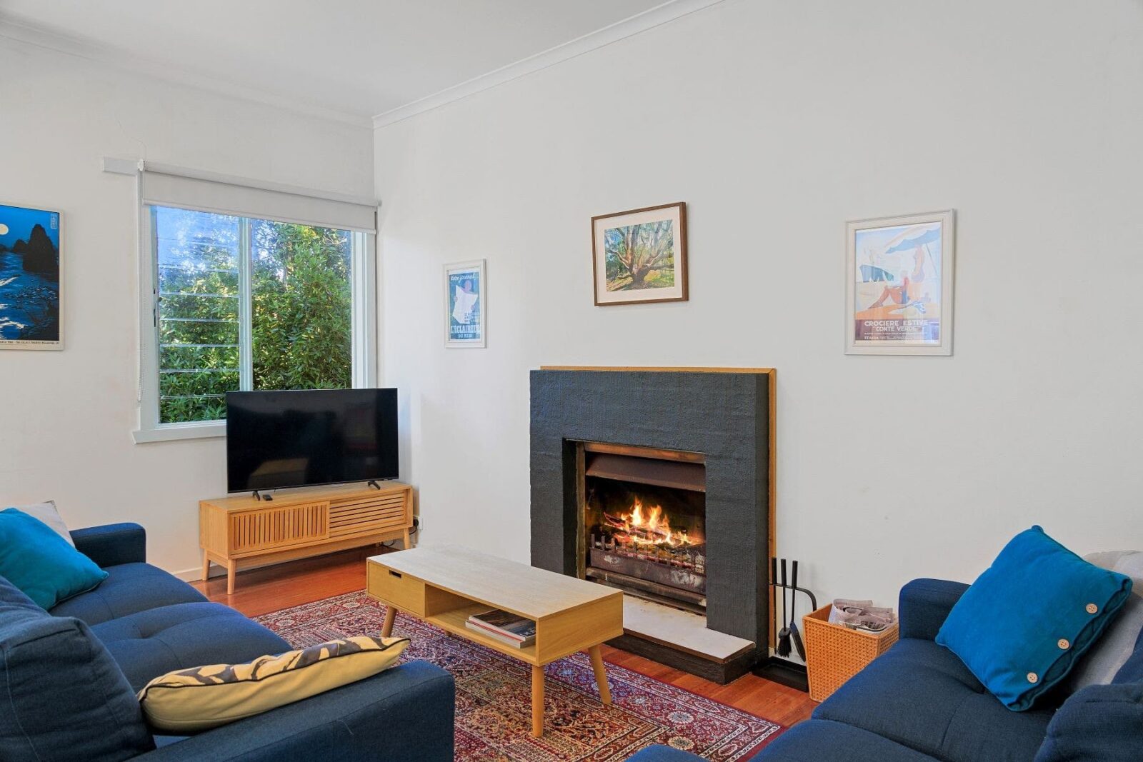 Lounge room with an open fireplace and two comfortable couches. Television beside window