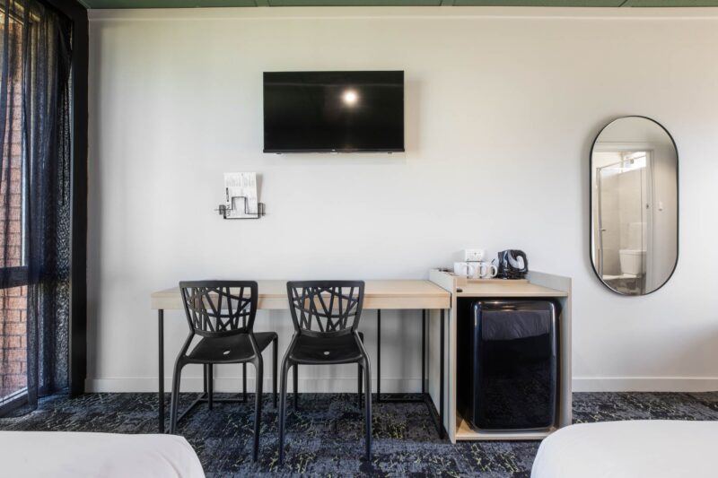 Hotel Room showing TV on the wall, fridge and two desk chairs pushed in at a desk