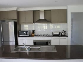 kitchen with island bench containing sink, looking to cooking area with white tile splashback