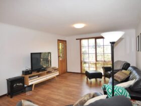 Living space at unit, timber floors, couch and armchairs, tv, ornamental fireplace & lamp