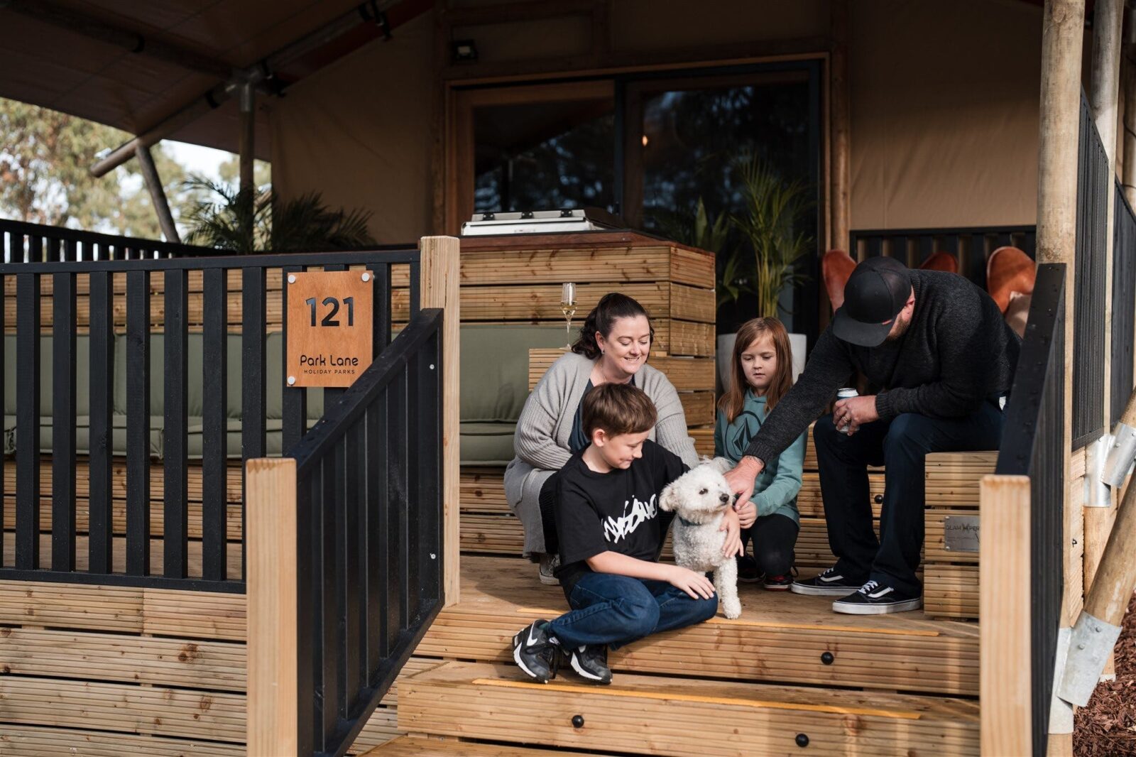Family sits on deck of safari tent with pet dog