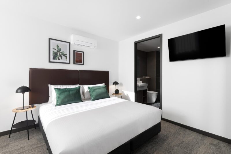 Quest Geelong Central apartment bedroom showing king bed with door open to ensuite bathroom