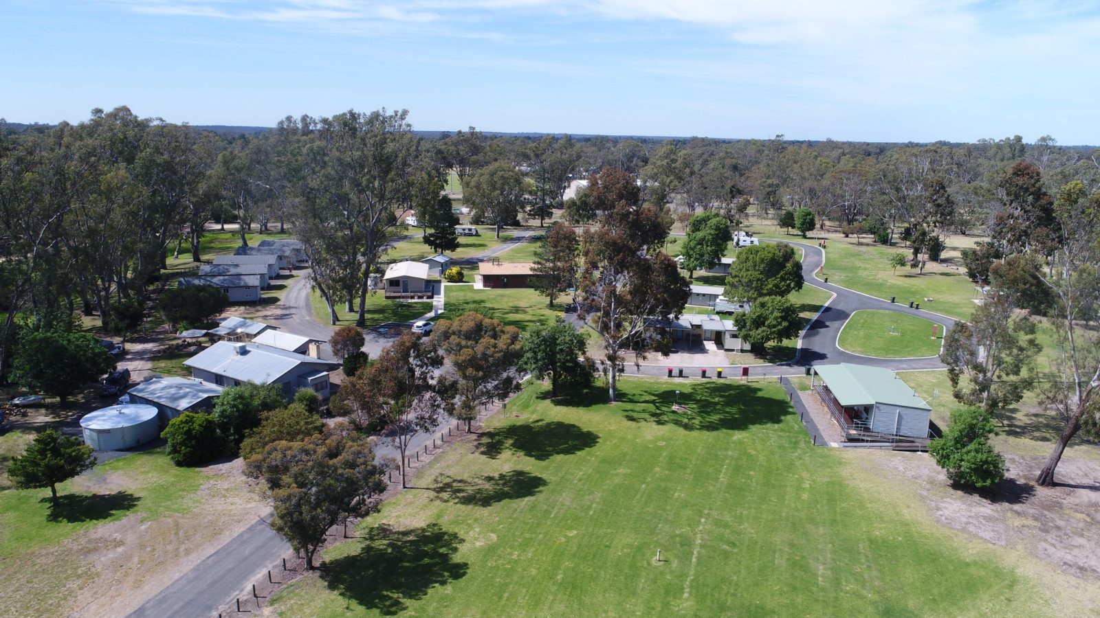 Overhead image of caravan park showing lawn areas, cabins, buildings, bushland and river at back