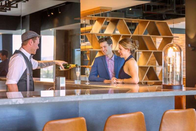 Bartender pouring sparkling wine to two guests at the bar