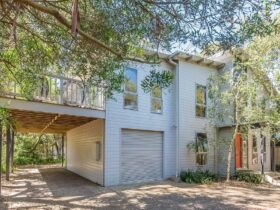 Image of double storey weatherboard home nestled amongst trees. Large upper level deck area.