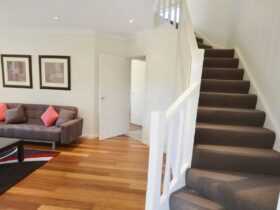 Image of staircase to upstairs on right, sitting room with timber floors on left, couch & floor rug