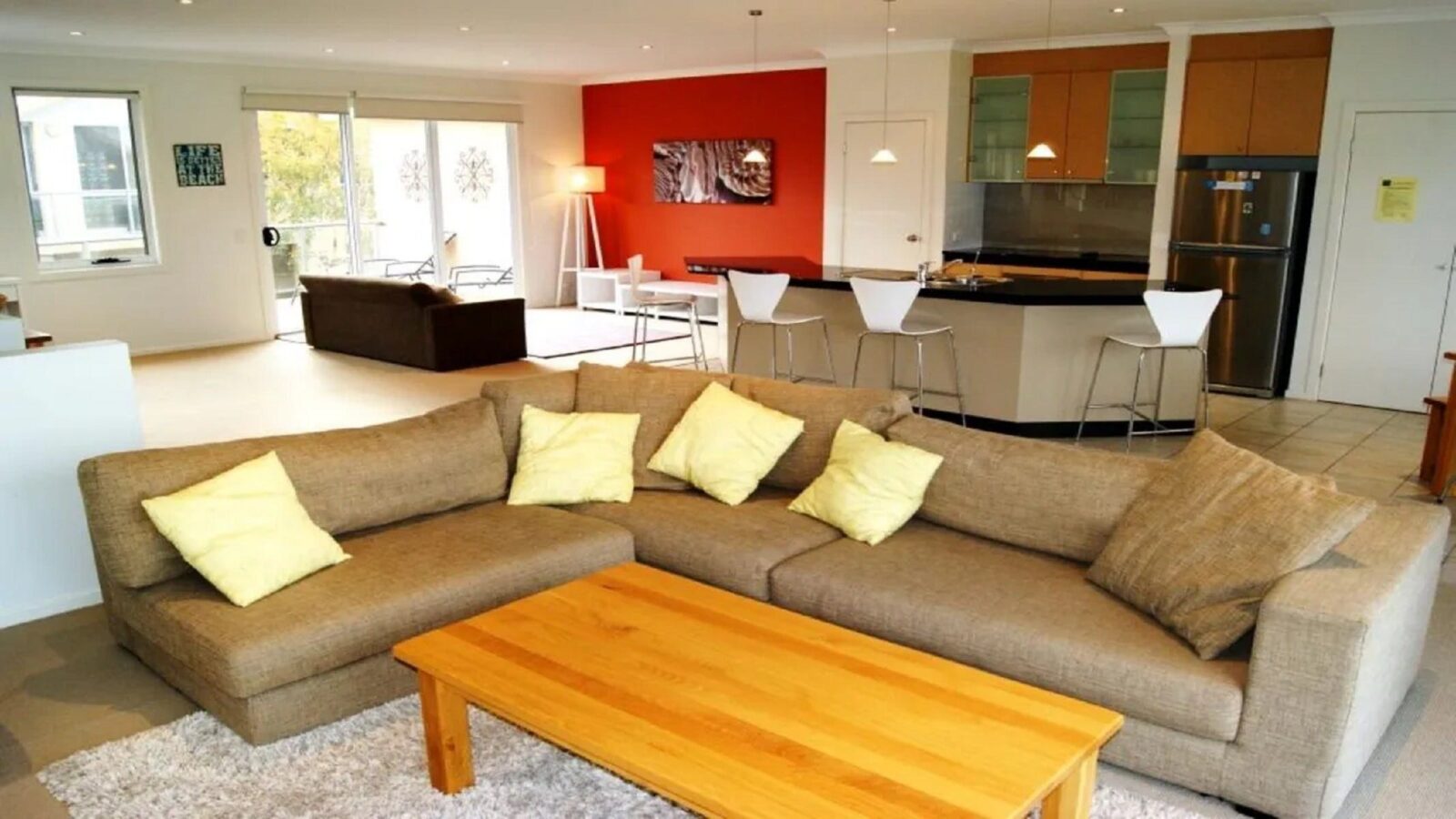 Image of living area with corner couch with kitchen meals area behind and sliding doors to balcony