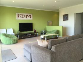 Lounge room with green feature wall, comfortable seating and tv unit. Stairway down to right.