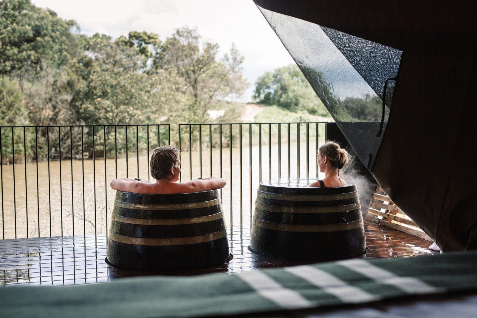 Man and woman bathing in hot springs barrels on their private glamping deck overlooking nature