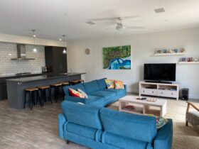Image of open plan living room with comfortable couches, kitchen with breakfast bar, television.