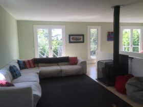 Living space with large corner couch, rug, enclosed wood heater door & windows to deck area