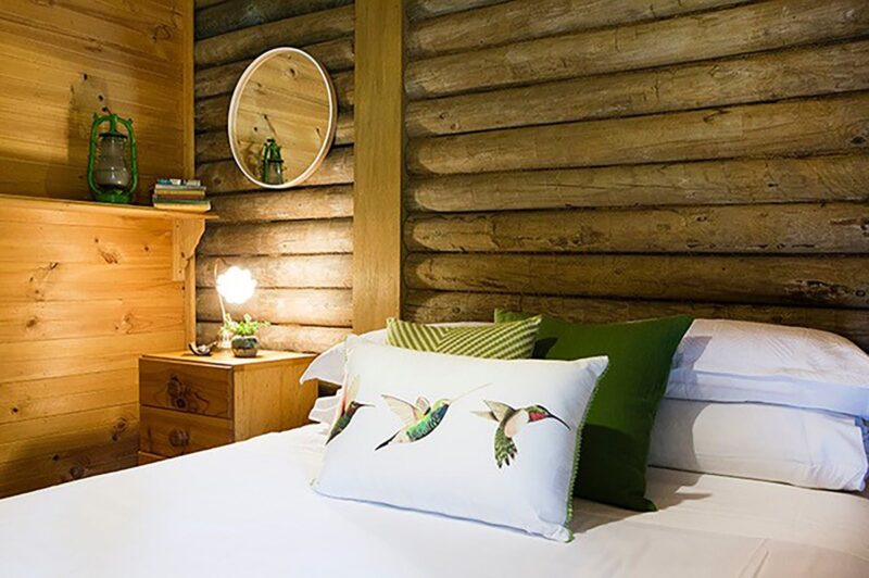 Second bedroom with exposed log walls, and a beautiful print of 3 birds on a white cushion
