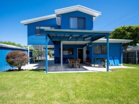Image of two storey blue weatherboard house with outdoor meals area downstairs and lawn area