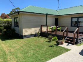 Image of front of weatherboard cottage showing steps up to deck with sitting area, lawn fron yard