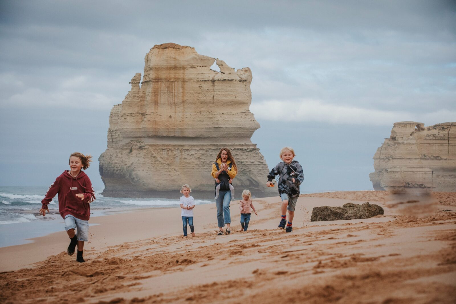 Family running along the beach at Gibson Steps with a rock stack in the background