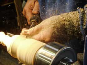 Spindle woodturning demonstration on a lathe showing chips flying from a chisel