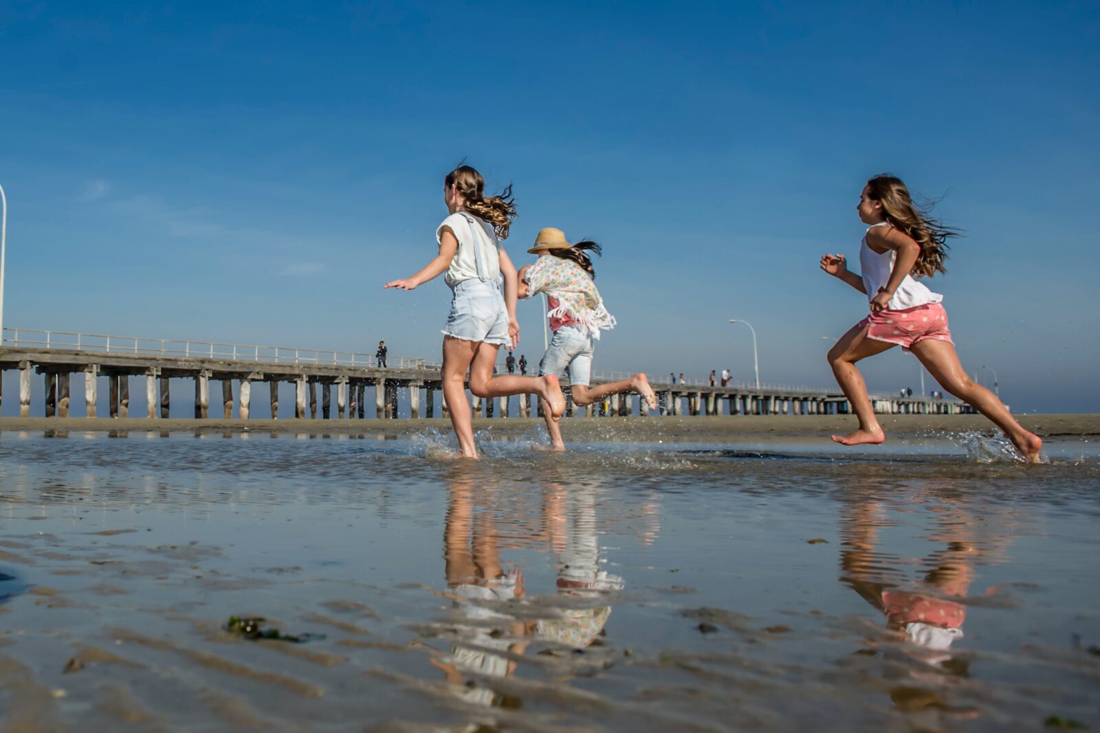 Children running at Altona Beach with Altona pier in the background.