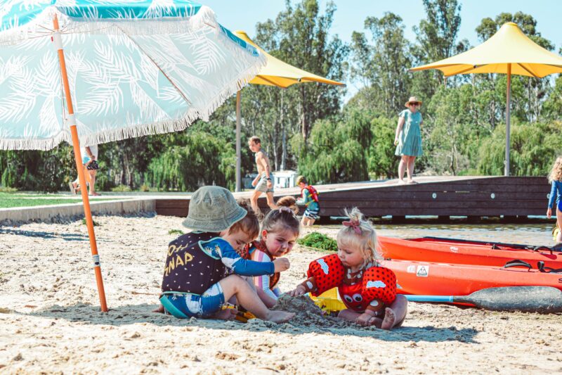 4 toddlers playing in the sand under a beach umbrella