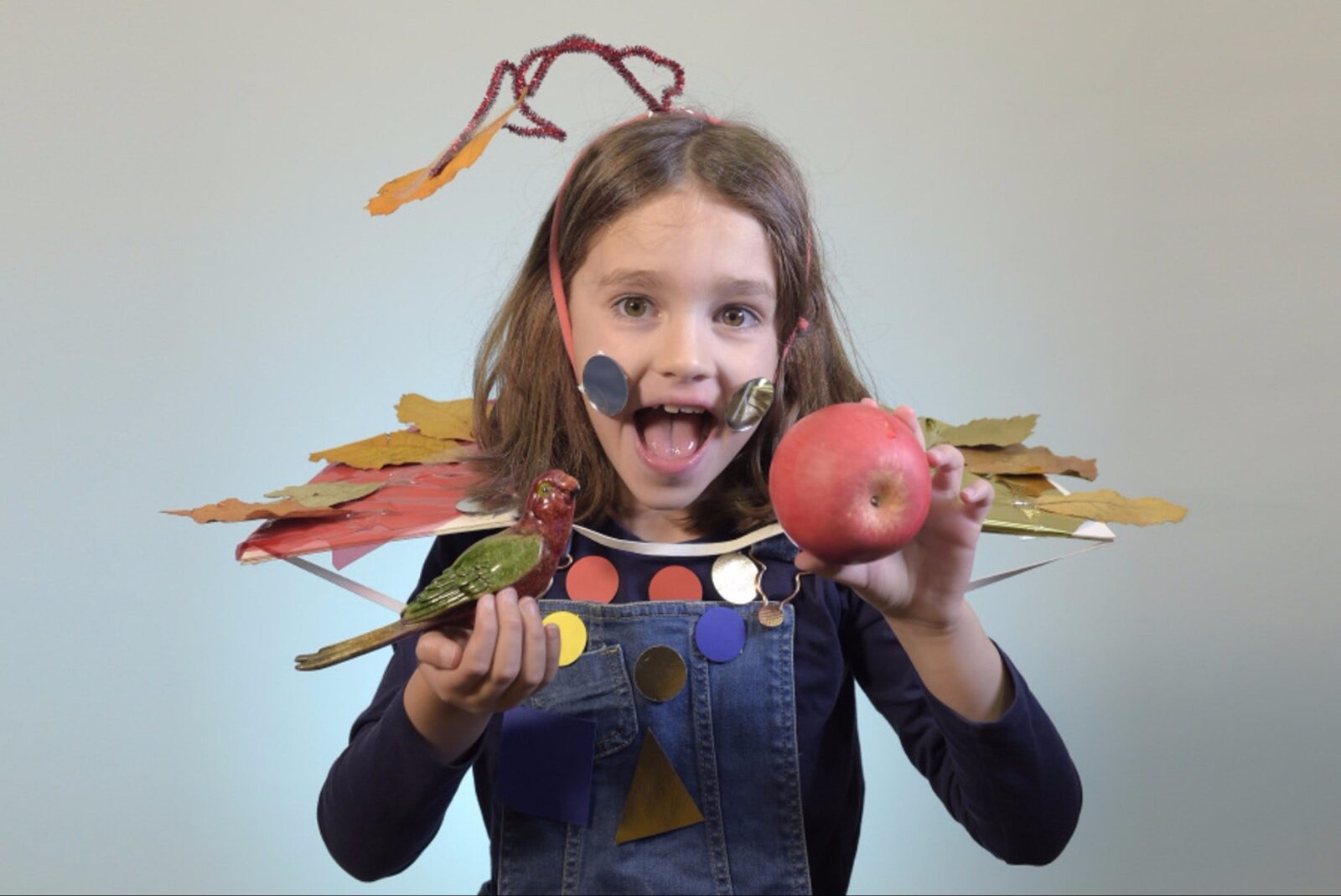 A little girl holding a porcelain bird and an apple on each hand