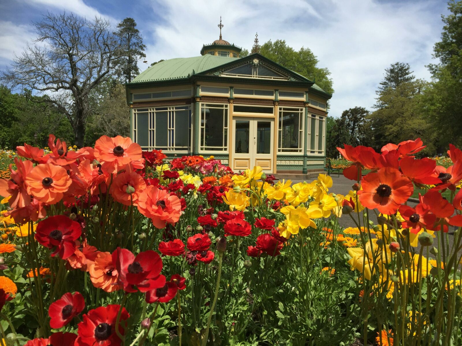 The statue pavilion sits behind a flower bed with yellow, red and orange flowers