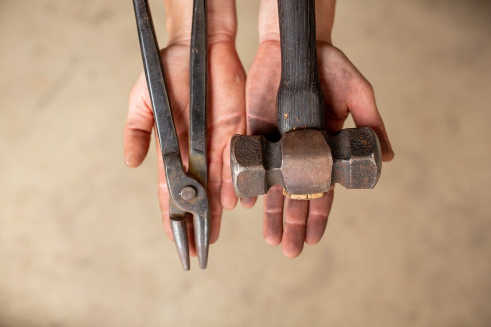 View from above of hands open flat holding a hammer and plyers